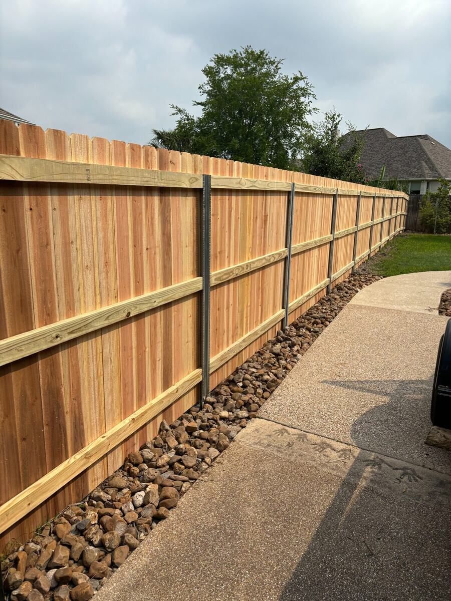 Cedar privacy fence with metal posts beside a curved walkway, completed by Tejas Construction