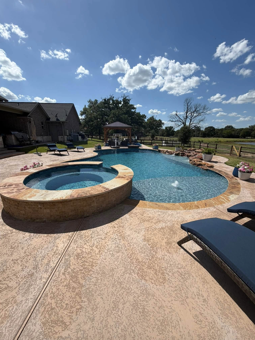 Freeform pool and spa with stamped concrete decking and travertine coping